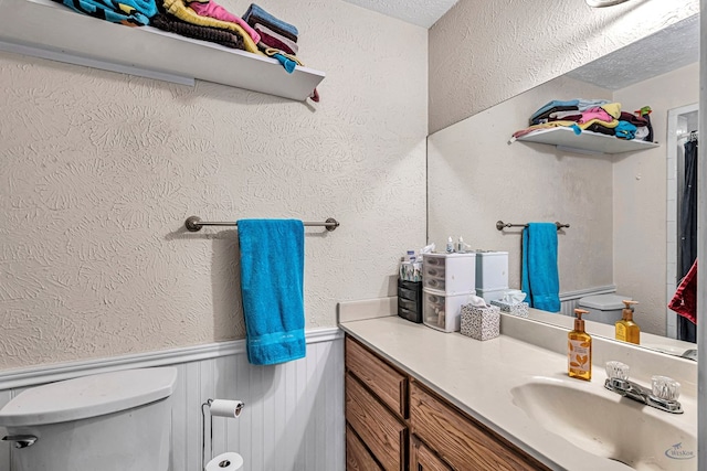 bathroom with wainscoting, toilet, vanity, and a textured wall