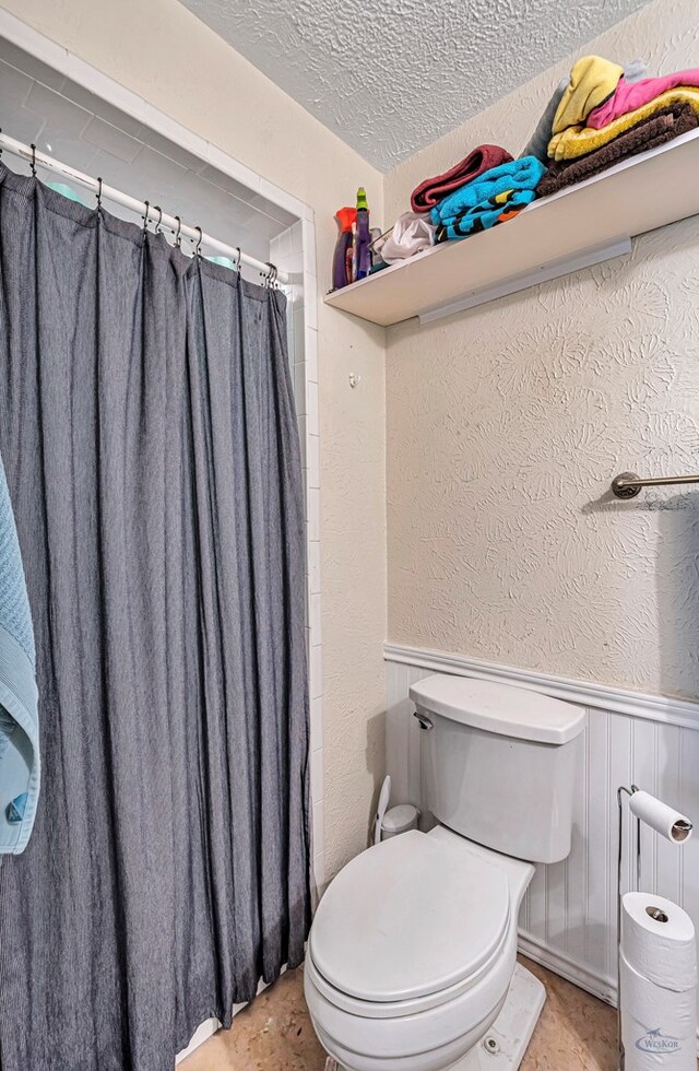 bathroom featuring wainscoting, a textured ceiling, toilet, and a textured wall