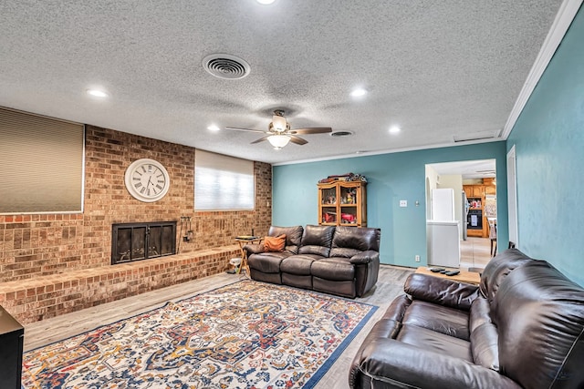 living area with visible vents, a ceiling fan, wood finished floors, a fireplace, and crown molding