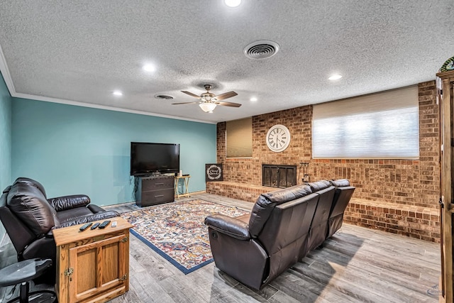 living room featuring visible vents, brick wall, light wood finished floors, ornamental molding, and ceiling fan