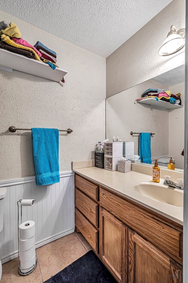 bathroom featuring vanity, a textured wall, a wainscoted wall, and a textured ceiling