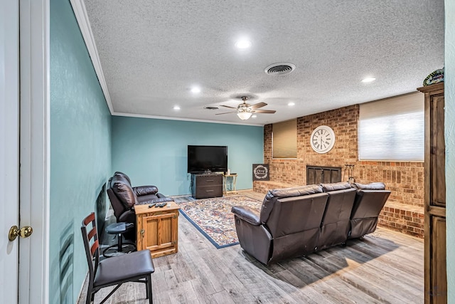 living area featuring visible vents, ornamental molding, light wood-style floors, a textured ceiling, and a ceiling fan