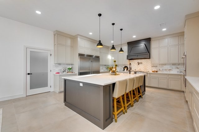 kitchen featuring a kitchen island with sink, a breakfast bar area, premium range hood, stainless steel built in fridge, and pendant lighting