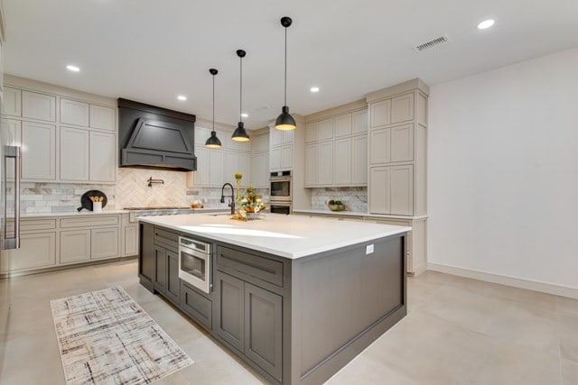 kitchen featuring pendant lighting, a large island with sink, custom exhaust hood, stovetop, and gray cabinetry