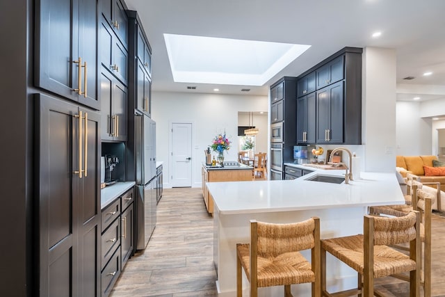 5807 Sterling Pl, Midland, TX 79707 - kitchen with a sink, light wood-style flooring, a skylight, a breakfast bar, and a peninsula
