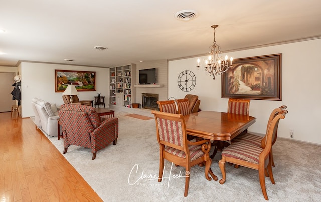 dining room with built in shelves, a large fireplace, visible vents, ornamental molding, and light wood-type flooring