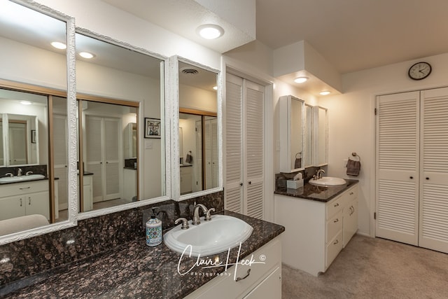 bathroom featuring a closet, two vanities, and a sink