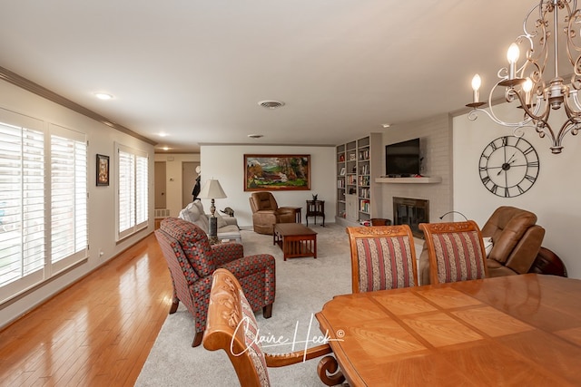 dining room featuring built in shelves, crown molding, light wood finished floors, visible vents, and a large fireplace