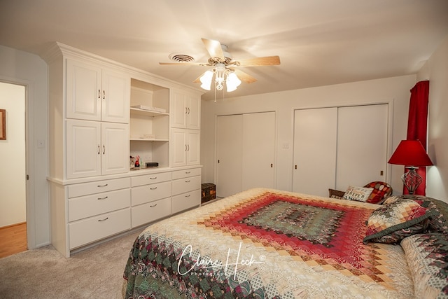 bedroom featuring light carpet, a ceiling fan, visible vents, and multiple closets