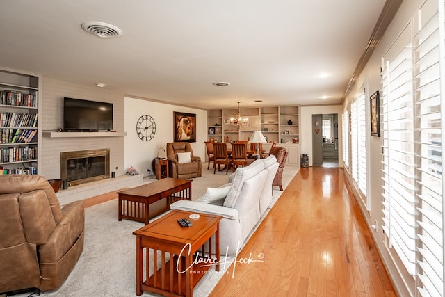 living area with visible vents, built in features, ornamental molding, a brick fireplace, and light wood finished floors