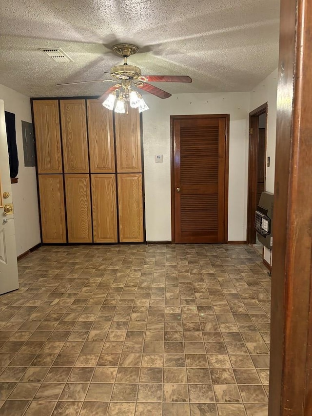 interior space featuring a textured ceiling, heating unit, ceiling fan, and electric panel