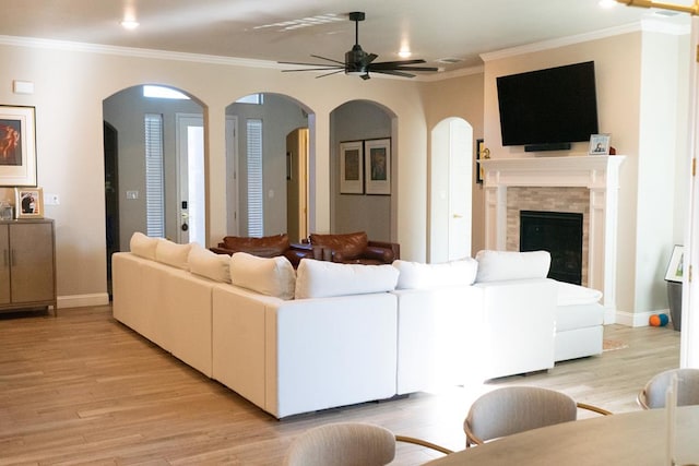 living room featuring ceiling fan, a tiled fireplace, crown molding, and light hardwood / wood-style flooring