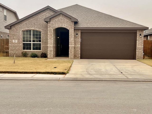 view of front facade featuring brick siding, a shingled roof, fence, driveway, and a front yard