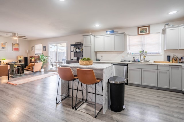 kitchen with light wood-type flooring, light stone countertops, sink, stainless steel dishwasher, and tasteful backsplash