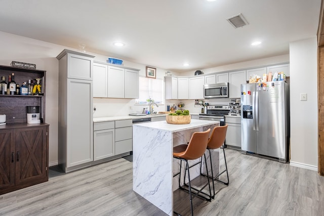 kitchen featuring stainless steel appliances, sink, a center island, a kitchen bar, and light hardwood / wood-style floors