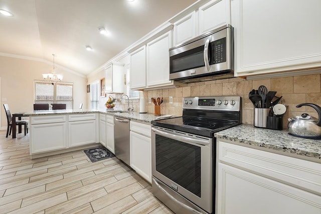 kitchen with ornamental molding, a peninsula, vaulted ceiling, stainless steel appliances, and a sink