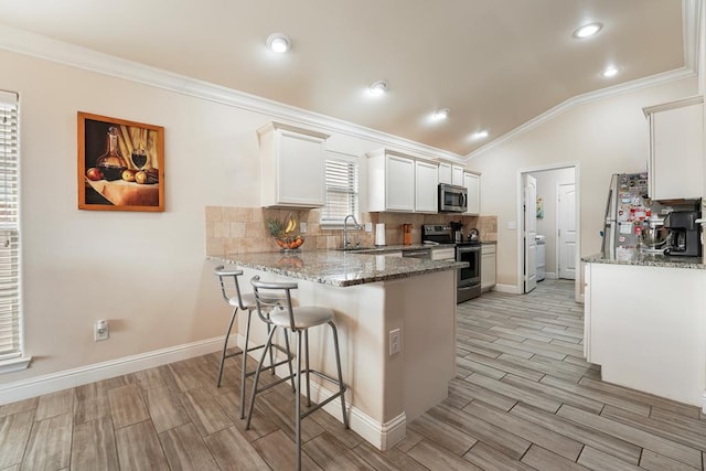 kitchen featuring a peninsula, a breakfast bar, a sink, appliances with stainless steel finishes, and decorative backsplash