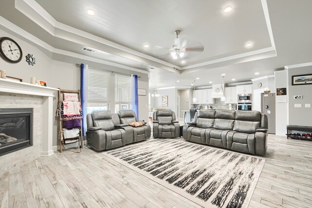 1706 Overshine Ln, Midland, TX 79705 - living area featuring a tray ceiling, ceiling fan, ornamental molding, a tiled fireplace, and light wood finished floors