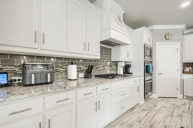 1706 Overshine Ln, Midland, TX 79705 - kitchen with custom range hood, stainless steel appliances, decorative backsplash, white cabinets, and light stone countertops