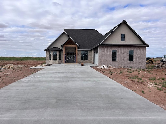 view of front of home with a garage, stucco siding, brick siding, and driveway