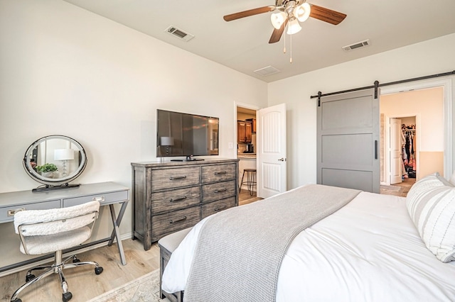 bedroom featuring a spacious closet, visible vents, light wood-style flooring, and a barn door