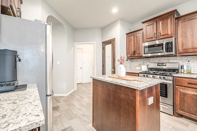 kitchen featuring light wood-type flooring, stainless steel appliances, a kitchen island, and decorative backsplash