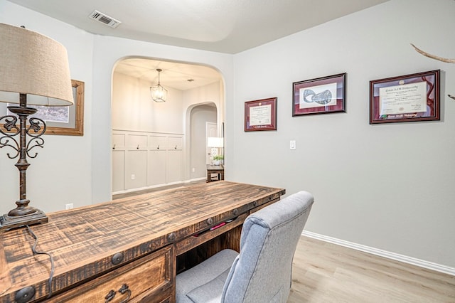 office area with baseboards, arched walkways, visible vents, and light wood-type flooring