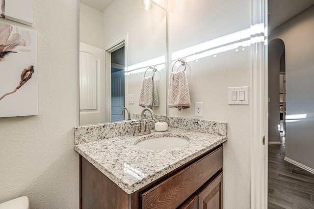 bathroom with baseboards, wood finished floors, vanity, and a textured wall