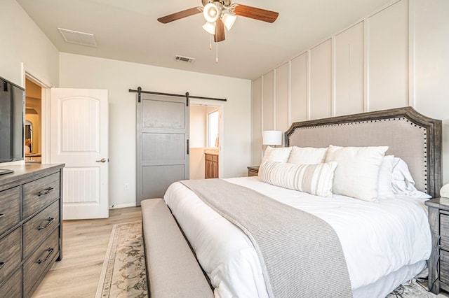 bedroom with a barn door, visible vents, ceiling fan, and light wood finished floors