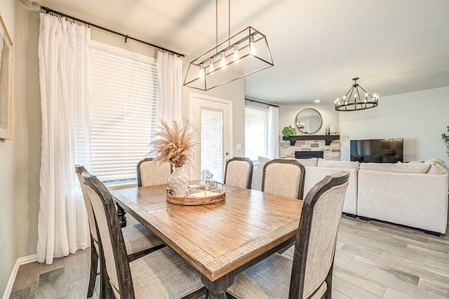 dining room featuring baseboards, a notable chandelier, a stone fireplace, and light wood-style flooring