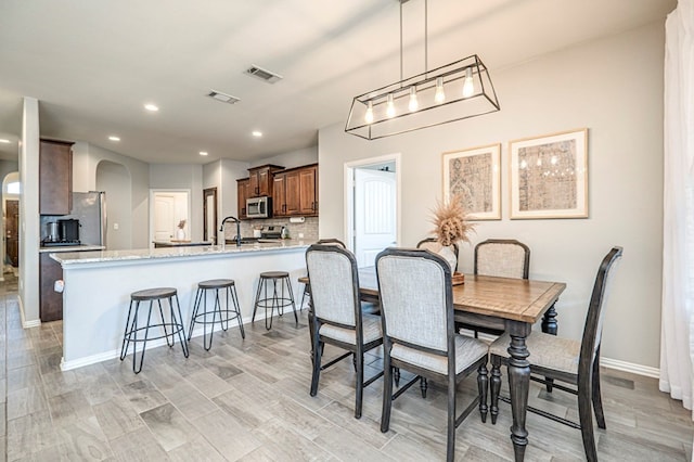 dining area with light wood-style flooring, recessed lighting, visible vents, and arched walkways