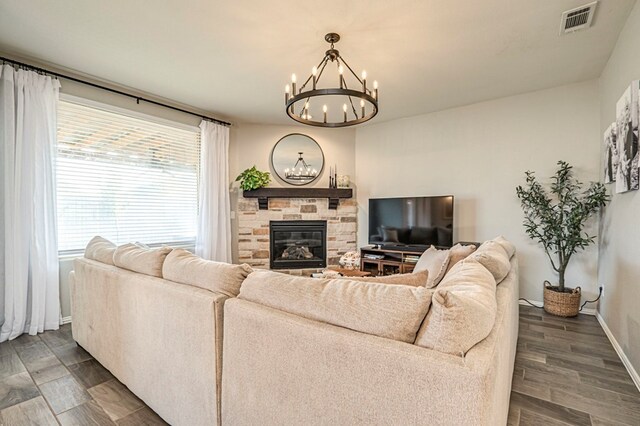 living room with baseboards, visible vents, dark wood-style flooring, a stone fireplace, and a notable chandelier