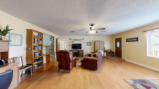 living area featuring light wood-style flooring, a textured ceiling, visible vents, and a ceiling fan