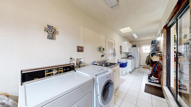 laundry area with a skylight, washing machine and clothes dryer, cabinet space, light tile patterned flooring, and a sink