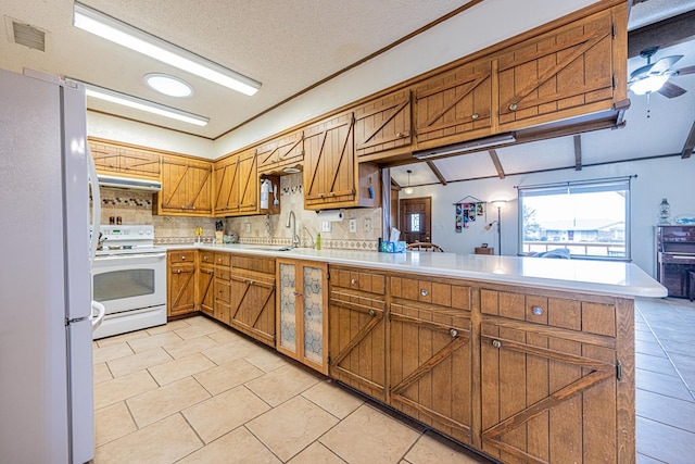 kitchen featuring white appliances, brown cabinetry, a peninsula, light countertops, and a sink