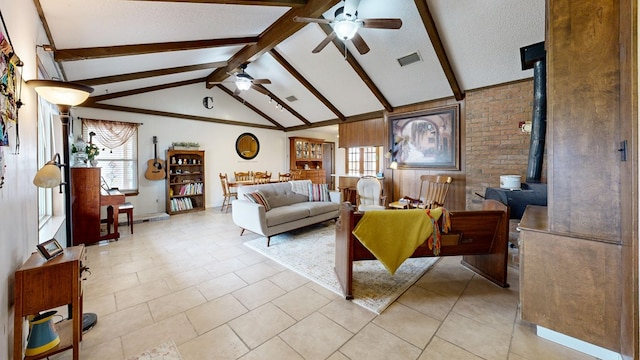 living area featuring vaulted ceiling with beams, visible vents, a wood stove, ceiling fan, and a textured ceiling