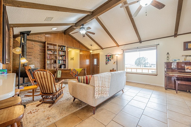 living area featuring lofted ceiling with beams, light tile patterned floors, a textured ceiling, a ceiling fan, and a wood stove