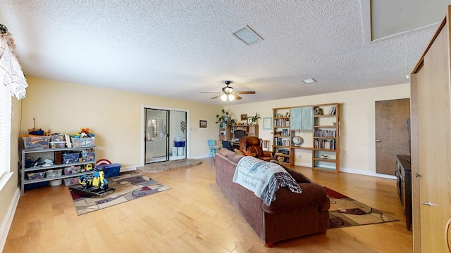 living room featuring a ceiling fan, a textured ceiling, visible vents, and wood finished floors