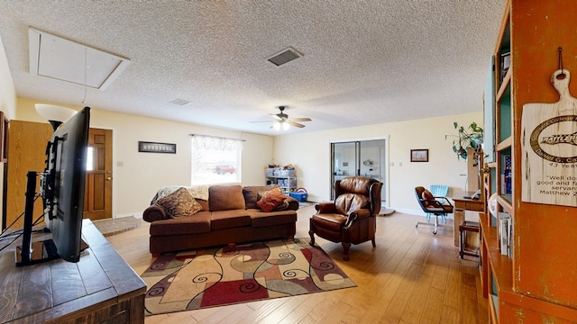 living area with a textured ceiling, wood finished floors, a ceiling fan, visible vents, and attic access