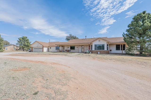 ranch-style home with brick siding, dirt driveway, a porch, board and batten siding, and a garage