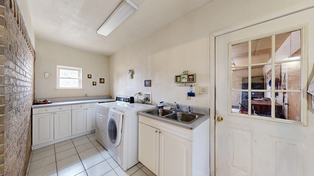 laundry area with light tile patterned floors, brick wall, a sink, cabinet space, and washing machine and clothes dryer