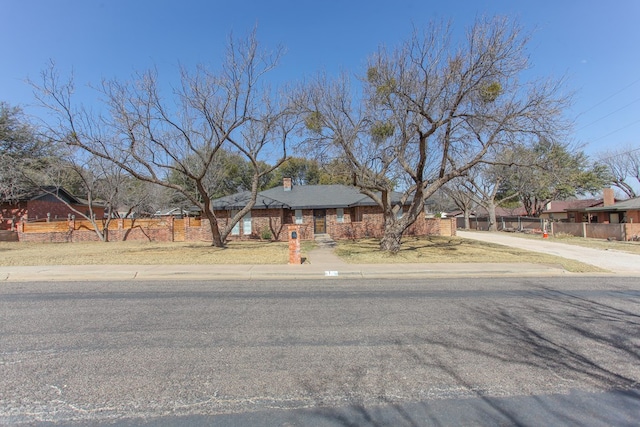 view of front of home with concrete driveway, a chimney, and fence