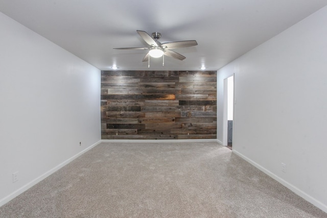 spare room with wooden walls, carpet, baseboards, ceiling fan, and an accent wall