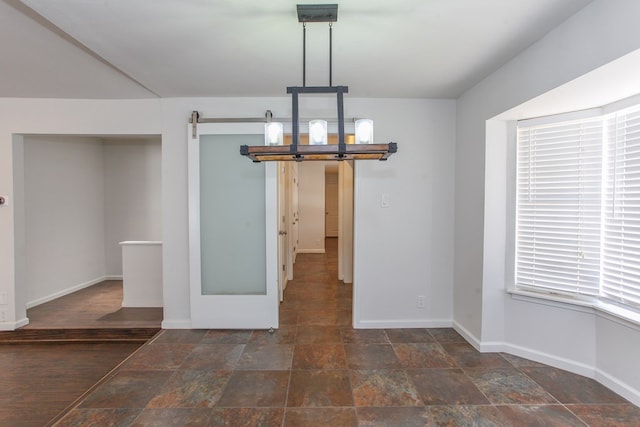 unfurnished dining area featuring a barn door, baseboards, and stone finish flooring