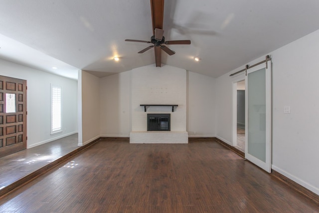 unfurnished living room with baseboards, lofted ceiling with beams, a barn door, a fireplace, and dark wood-style floors