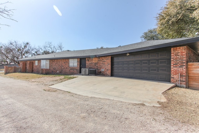 ranch-style house with brick siding, fence, concrete driveway, central AC unit, and an attached garage