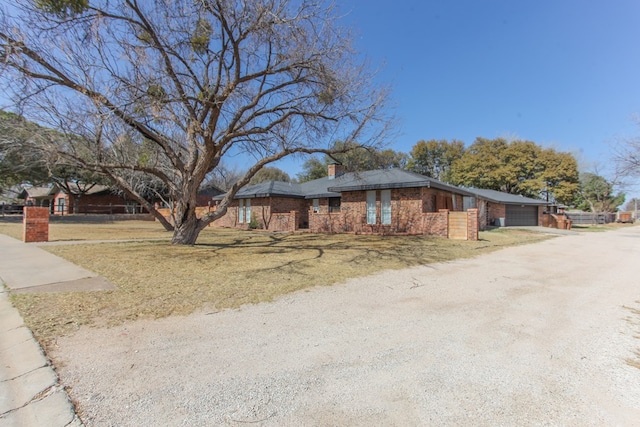 view of side of property featuring driveway, a yard, a chimney, a garage, and brick siding