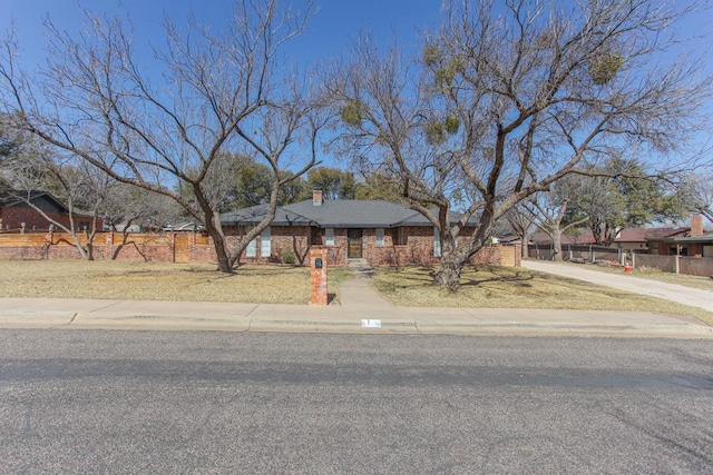 view of front of house with fence, brick siding, driveway, and a chimney