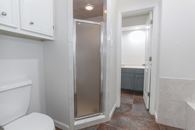 bathroom with stone tile flooring, a stall shower, toilet, and vanity