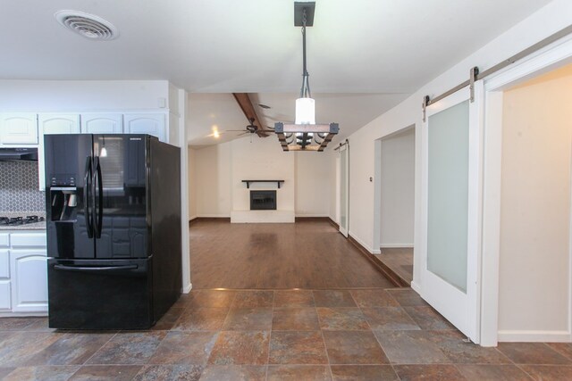 kitchen with visible vents, a fireplace with raised hearth, a ceiling fan, under cabinet range hood, and black refrigerator with ice dispenser